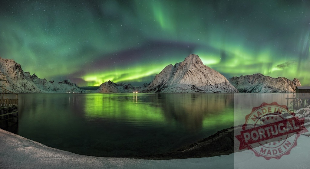 Northern lights aurora borealis visible over snowy Lofoten fjord | Green aurora borealis reflecting on still water surrounded by snow-covered mountains - Realized with Pictrs.com