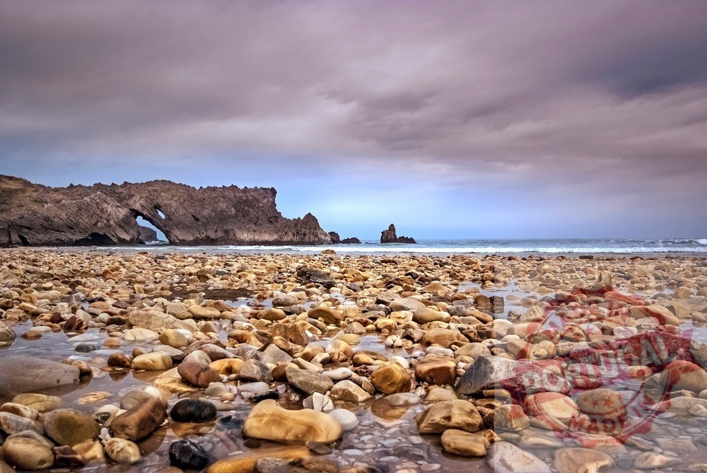Portizuelo beach, Cantabria, Spain with natural sea arch | Pebble beach with ocean waves breaking under a sea arch on a cloudy day - Realisiert mit Pictrs.com
