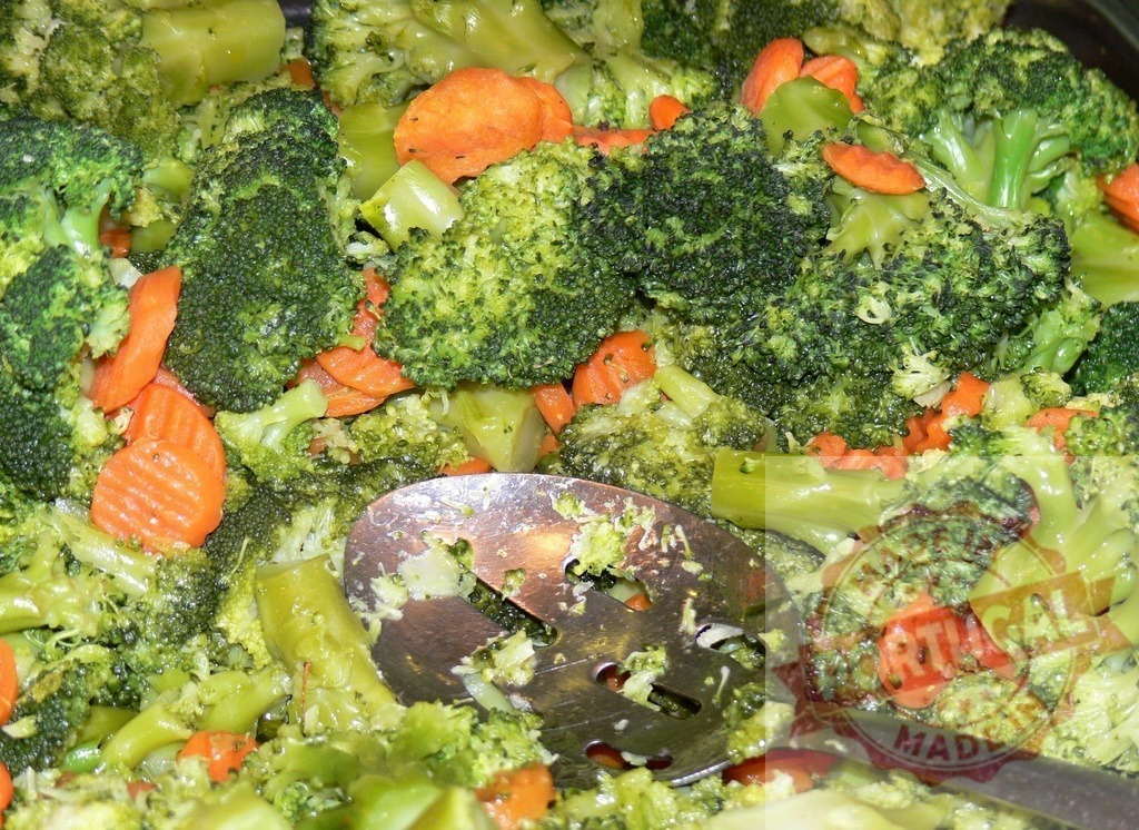 Steamed broccoli and sliced carrots vegetable medley with serving spoon | Cooked broccoli florets and carrot slices mixed together, ready for serving - Realized with Pictrs.com