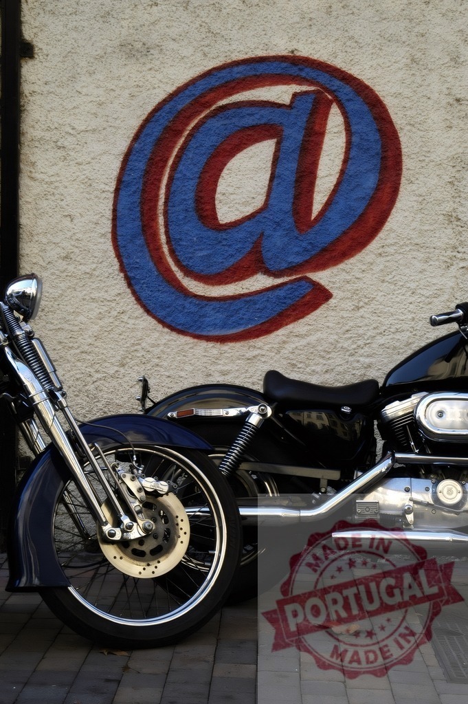 Motorcycle parked against wall with painted at symbol | Motorbike standing on a street next to a wall with a blue and red internet symbol - Realisiert mit Pictrs.com
