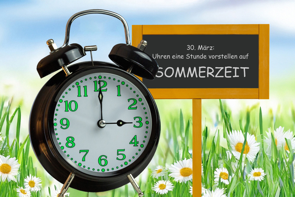 Zeitumstellung 2026: Schild, Wecker und (K.I.-generierte) Frühlingswiese | (Fotomontage) Zeitumstellung Sommerzeit Symbolbild: Wecker vor einer Blumenwiese und Text 30. MÄRZ UHREN UMSTELLEN AUF SOMMER - Realisiert mit Pictrs.com