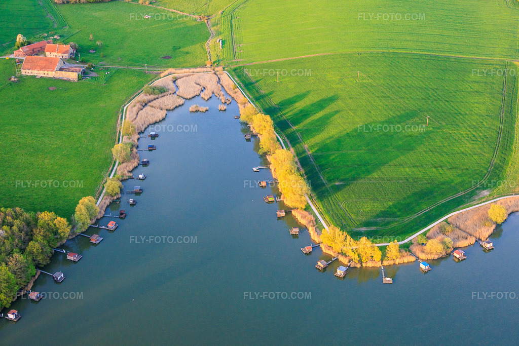 Aerial view: Boardwalks with fishing huts line the shore of Lake Etang du Welschhof. in Puttelange-aux-Lacs in the state Moselle, France. – Photo: IMG_154402.jpg taken on 04/17/2026 by Werner Riehm/FLY-FOTO.com – Resolution of the original: 6000 x 4000 px