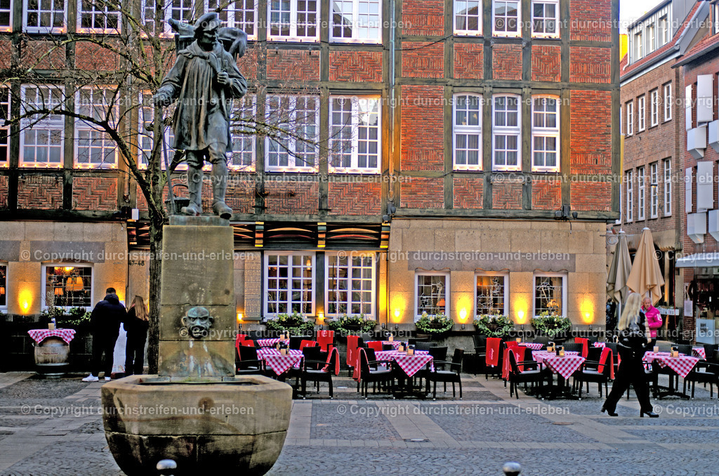Kiepenkerl auf dem Brunnen Münster | Der Kiepenkerl in Münster ist ein bekanntes Wahrzeichen der Stadt. Er steht im Kiepenkerlviertel am Spiekerhof.an einem kleinen Wasserbecken bzw. einer Brunneneinfassung. und repräsentiert westfälischen Wanderhändler (Kiepenkerle), die einst mit ihrer Rückentrage (Kiepe) Waren wie Eier, Butter und Geflügel vom Land in die Stadt brachten. Ein ursprüngliches Denkmal August Schmiemanns (1896) wurde im Zweiten Weltkrieg zerstört. Die heutige Bronzestatue ist ein Nachguss aus dem Jahr 1953. Der Mann trägt die typische Tracht: einen blauen Leinenkittel, ein rotes Halstuch, eine Mütze und einen Wanderstab.. Hier raucht er eine Pfeife. - Realisiert mit Pictrs.com