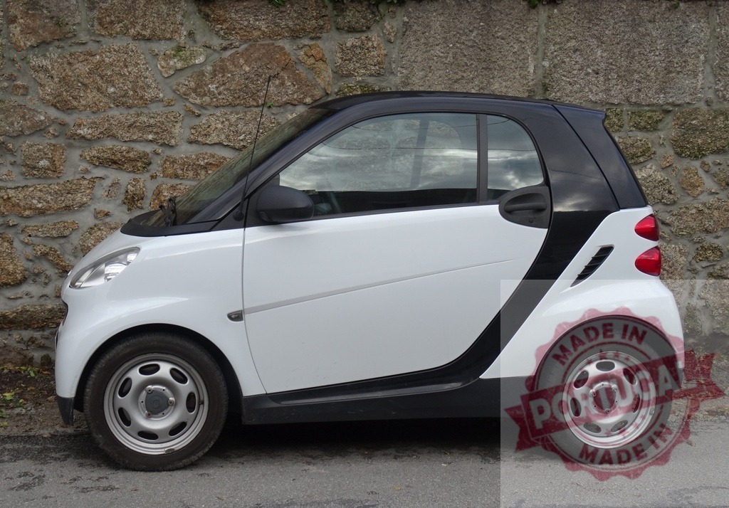 Smart car parked on street beside stone wall | White and black Smart car parked outdoors, representing compact urban transport - Realized with Pictrs.com