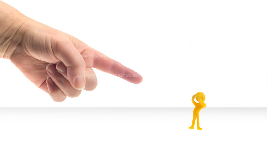 Symbolbild zeigt wie Mobbing geschieht | Eine Person zeigt mit dem Zeigefinger auf ein kleines Männchen. Das Männchen schläft die Hände bestürzt vor die Augen. Symbolbild für Mobbing, weißer Hintergrund. 