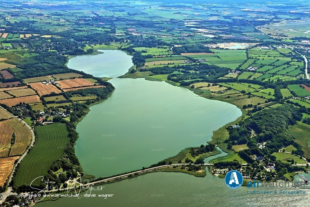 In der Blütezeit im 10. Jahrhundert lebten schätzungsweise 1.000 bis 2.000 Menschen in der Stadt Haithabu - Luftbild | In der Blütezeit im 10. Jahrhundert lebten schätzungsweise 1.000 bis 2.000 Menschen in der Stadt, die als Schmelztiegel verschiedener Kulturen (Dänen, Sachsen, Friesen, Slawen) diente und weitreichende Handelsnetze bis nach Byzanz und in den Nahen Osten unterhielt.  Der Schutz der Stadt erfolgte durch einen befestigten Halbkreiswall, der im Westen direkt an das Verteidigungssystem des Danewerks anschloss.