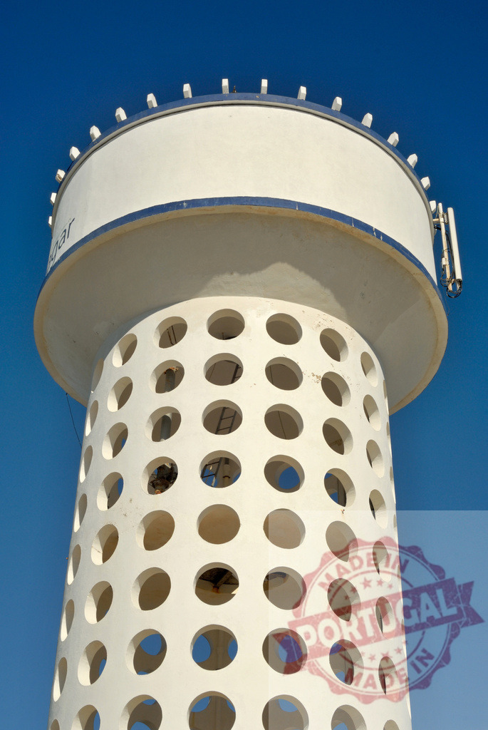 Modern concrete water tower structure against clear sky | White cylindrical water tower with circular holes rising into a deep blue sky - Realized with Pictrs.com