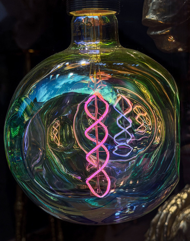Neon-Helix – Abstraktes Irisierendes Lichtkunst Wandbild | Ein faszinierendes Meisterwerk moderner Lichtästhetik. Diese detailreiche Fine-Art-Fotografie fängt das spektakuläre Leuchten einer Design-Glühbirne ein. Die pinkfarbene, helixartige LED-Struktur im Inneren kontrastiert perfekt mit den schillernden Regenbogenfarben der organisch geformten Glashülle. Ein hochexklusiver, futuristischer Eyecatcher, der lebendige Farben und modernen Cyberpunk-Charme in minimalistische Wohnräume, Lofts oder kreative Studios bringt. Empfohlen als Großformat unter Acrylglas für maximale Tiefenwirkung. - Realisiert mit Pictrs.com