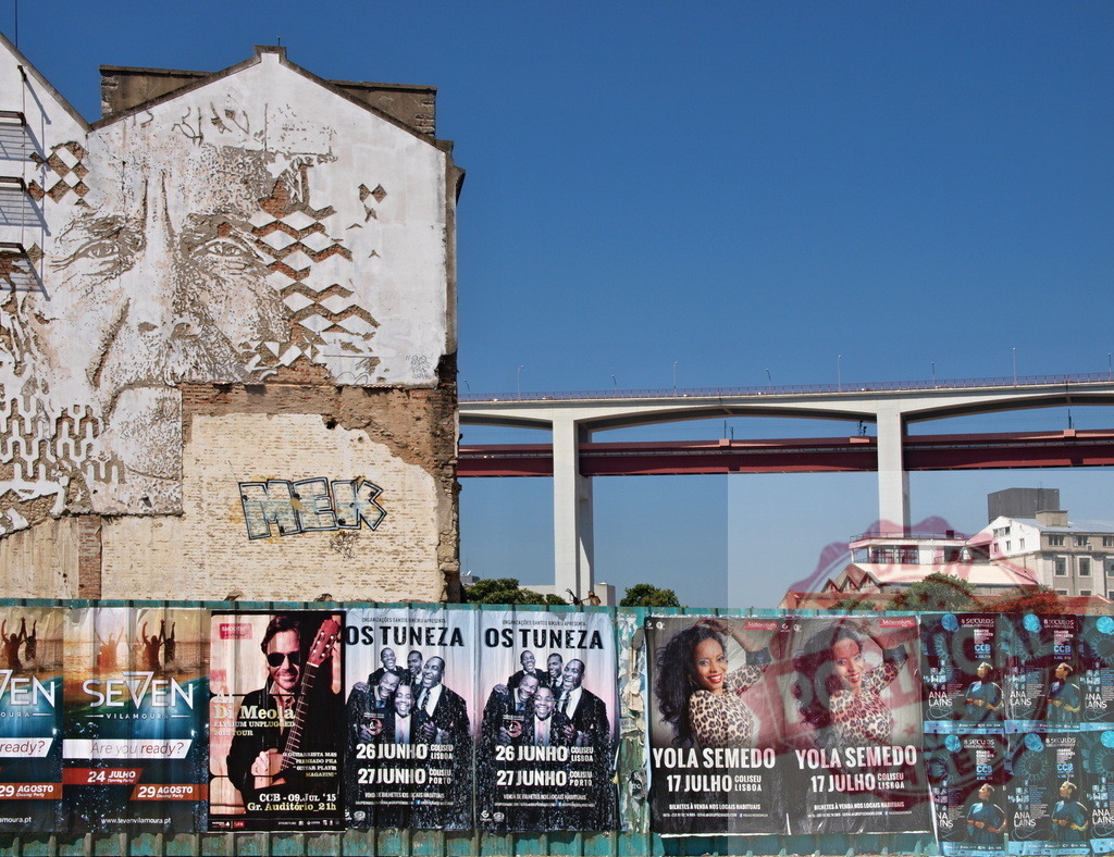 Vhils urban street art mural in Lisbon. Lisbon - Portugal | Vhils street art mural on building facade with concert posters and 25 de Abril Bridge - Realized with Pictrs.com