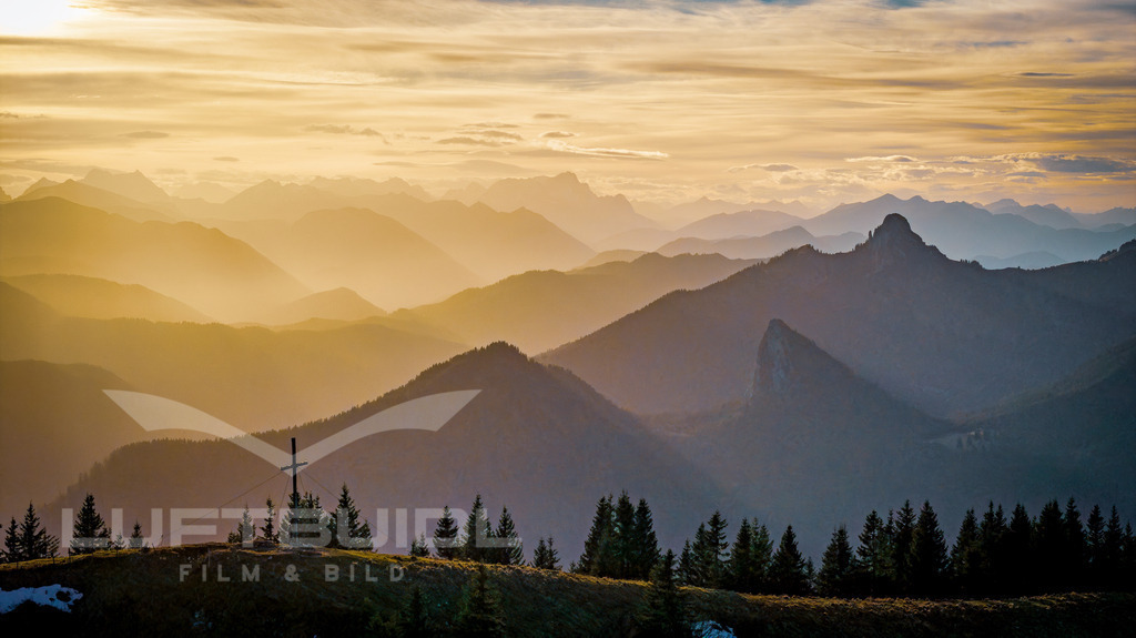 Setzberg im Saharastaub; H57 | Blick vom Setzberggipfel über Leonhardstein, Grüneck, Ross- und Buchstein Richtung Zugspitze. Der Saharastaub der letzten Tage schwängert die Luft in orangenen Tönen und sorgt so für erhebliches Streulicht. Im Gegenlicht der Sonne verschwinden die Tiefen des Vordergrundes. - Realisiert mit Pictrs.com