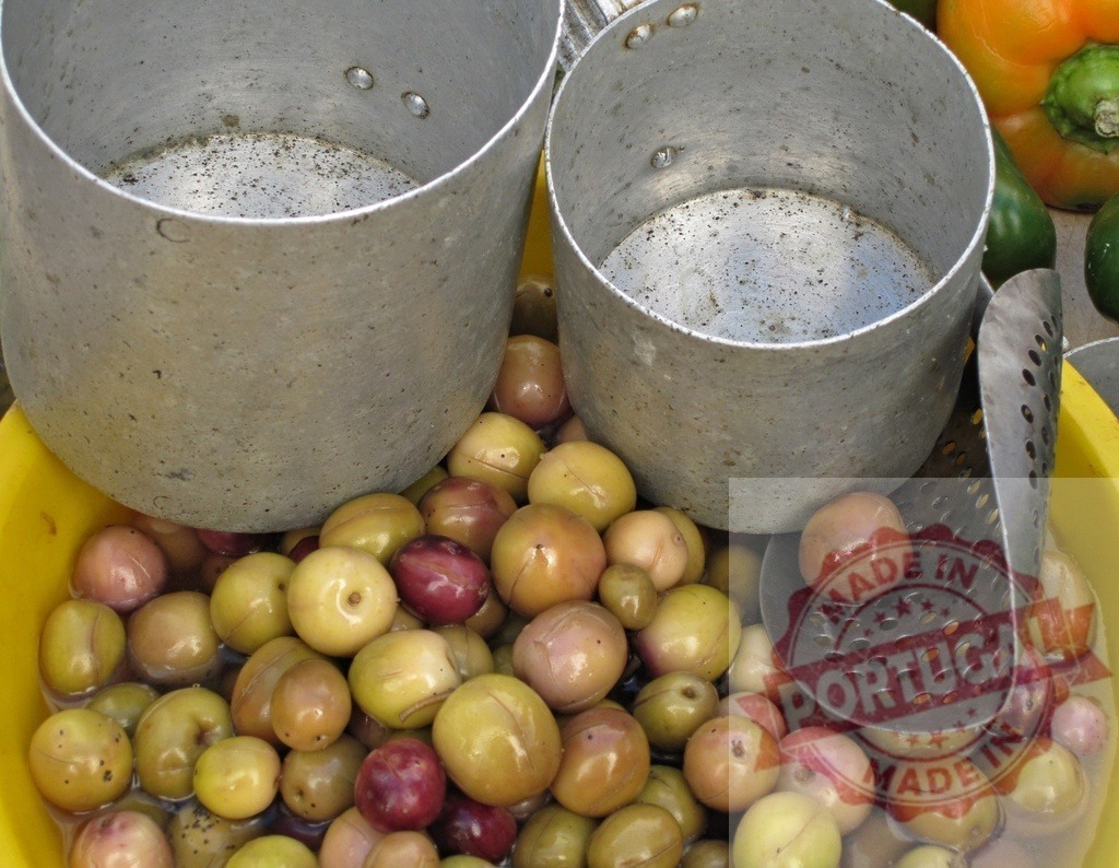 Olives in brine with metal pails and slotted spoon | Olives soaking in liquid, displayed in a yellow bowl with metal containers and a serving spoon - Realisiert mit Pictrs.com