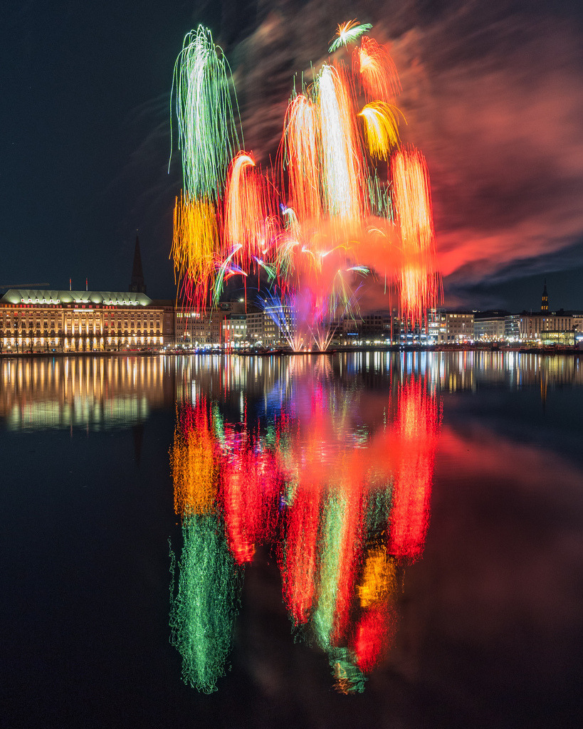 Farben über der Hamburger Alster | Ein außergewöhnliches Feuerwerk taucht Himmel und Wasser in intensive Grün-, Rot- und Orangetöne. Die langen Lichtspuren und Spiegelungen erzeugen eine fast abstrakte Ansicht Hamburgs. - Realisiert mit Pictrs.com