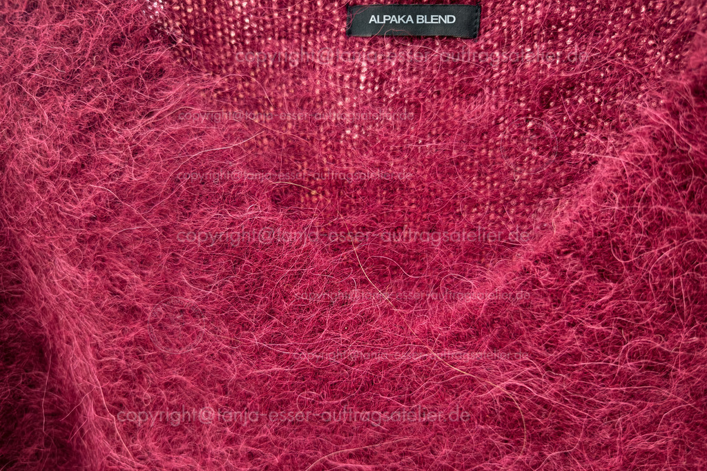 Alpaka Pullover D | Leuchtend bordeauxfarbener V Ausschnitt Pullovers mit einem Etikett, das den englischen Text Alpaka Mischung kennzeichnet. Die Oberfläche ist flauschig und mit langen Fasern, charakteristisch für Alpakamischungen. 