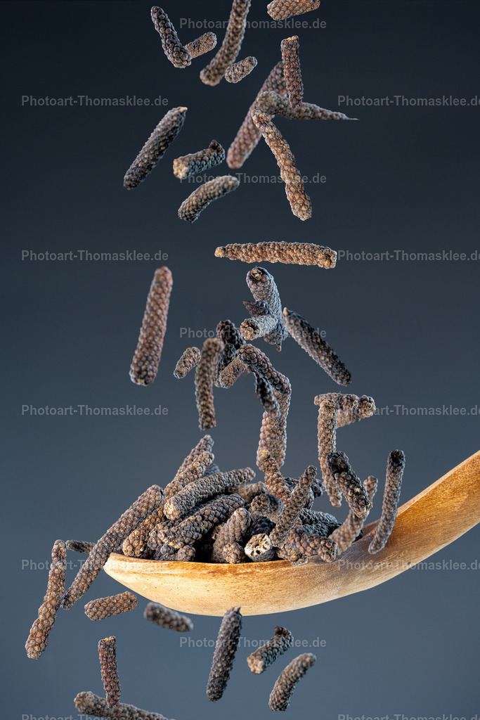 Langer Pfeffer – Würzig und aromatisch | Langer Pfeffer – Würzig und aromatisch. Kollektion: A spoon of tastefully seasonings.In dieser faszinierenden Studioaufnahme fällt langer schwarzer Pfeffer – auch Langpfeffer genannt – wie kleine dunkle Zylinder von oben herab auf einen rustikalen Holzlöffel. Durch die Verwendung von Highspeed-Blitzen wird der Moment der Bewegung gestochen scharf eingefroren, sodass jede Struktur und jede einzelne Pfefferfrucht sichtbar wird. Der Hintergrund zeigt einen dunklen blaugrauen Farbverlauf, der den rauen Charakter des Holzlöffels und die intensive Textur der Gewürze perfekt hervorhebt. Das Bild verbindet natürliche Eleganz mit dynamischer Ästhetik und bietet sich ideal als hochwertiges Dekorationselement sowohl für private Küchen als auch für gastronomische oder gewerbliche Räume an.Wo könnte man dieses Bild am besten aufhängen?Privater Bereich:In der Küche über einer Gewürztheke oder Arbeitsfläche als stilvolles Food-Statement.Im Esszimmer als harmonisches Kunstobjekt für Genussmenschen.Gewerblicher Bereich:In einem Feinkostladen oder Gewürzgeschäft als stimmungsvolle Präsentation hochwertiger Produkte.In Restaurants, besonders in solchen mit internationaler oder gehobener Küche, als exklusives Wandbild.Alu-Dibond: Perfekt für eine moderne, stilbewusste Einrichtung – klare Details und matte Oberfläche unterstreichen die natürliche Struktur des langen Pfeffers.Acrylglas: Verleiht den dunklen Pfefferzylindern eine faszinierende Tiefenwirkung und lässt den Hintergrund samtig elegant erscheinen.Poster: Ideal für flexibles, leichtes Dekor – bringt eine natürliche Atmosphäre in Küchen und gewerbliche Räume.Leinwand: Die leicht strukturierte Oberfläche der Leinwand harmoniert wunderbar mit dem rustikalen Charakter des Holzlöffels und verstärkt den natürlichen Eindruck des Motivs. - Realisiert mit Pictrs.com
