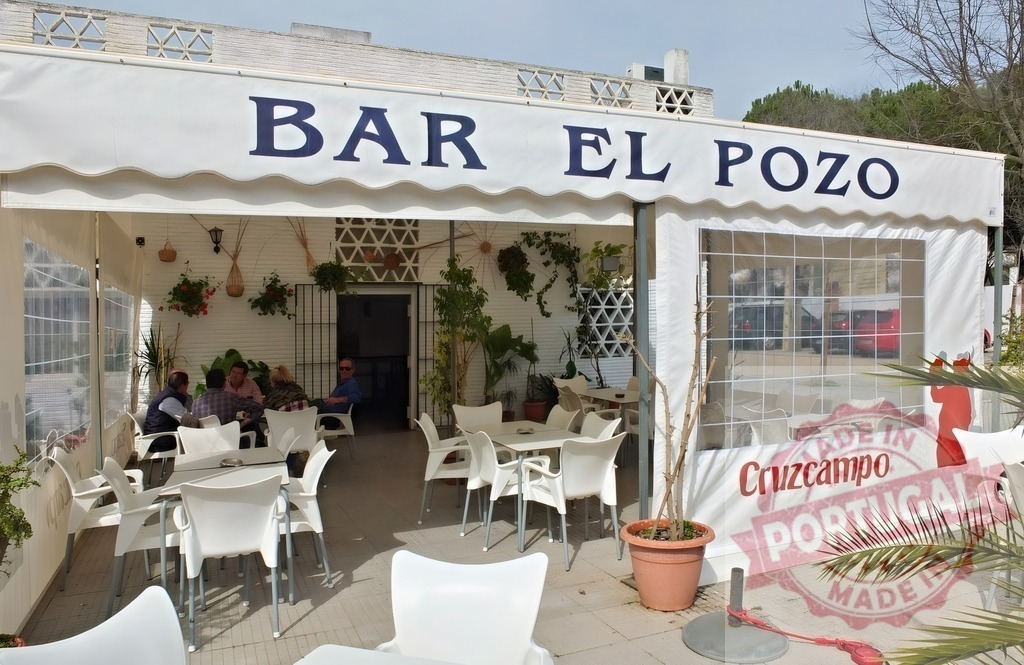 People enjoying a beverage at Bar El Pozo terrace in Spain | Customers relaxing at an outdoor Spanish bar and restaurant in sunlight - Realized with Pictrs.com