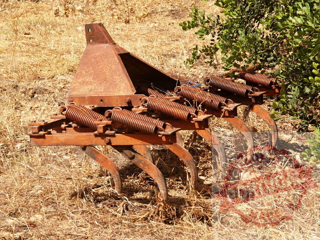 Rusty old farm implement resting in dried field | Rusty vintage cultivator sitting in dry rural field - Realized with Pictrs.com