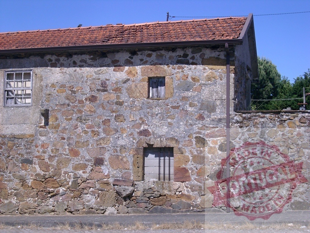Old rustic stone house with red roof tiles. Portugal - Norte | Building with ancient stone wall and vintage roof tiles under clear blue sky - Realized with Pictrs.com