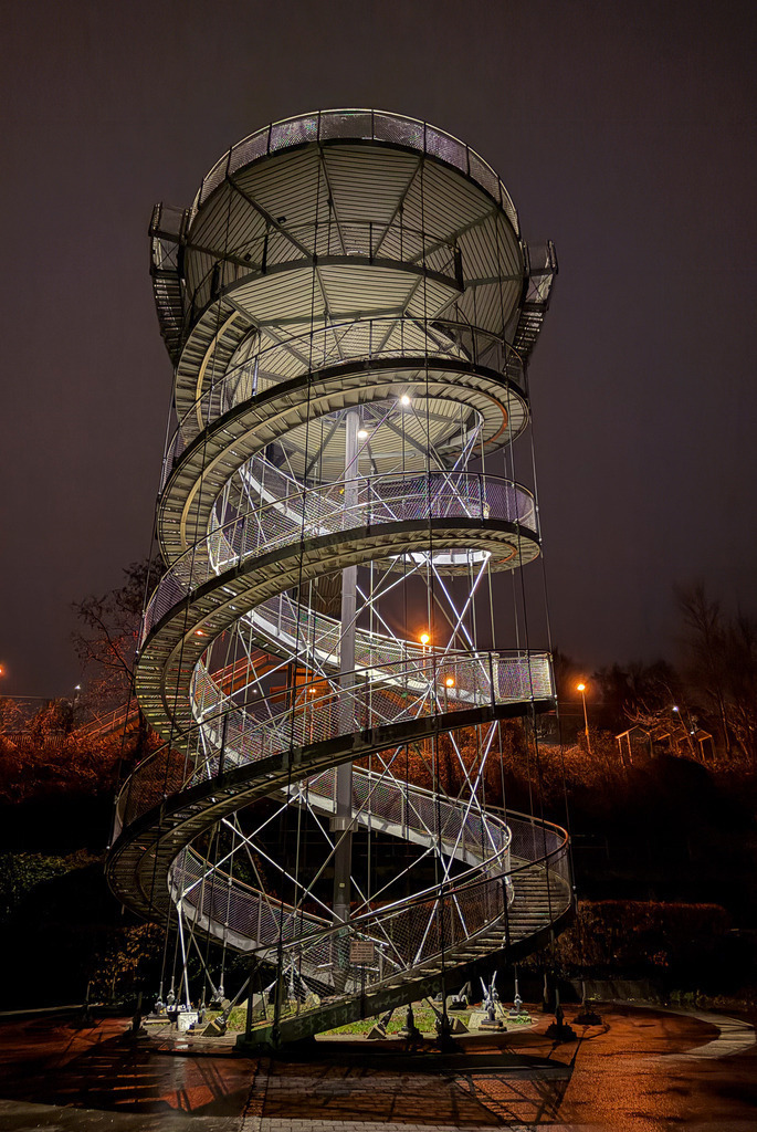 Architektonische Geometrie: Der illuminierte Spiralturm bei Nacht | Symmetrie, Dynamik und nächtliche Eleganz vereint in einem faszinierenden Architektur-Kunstwerk. Diese präzise Fotokunst-Aufnahme des spiralförmigen Turms besticht durch ihre klaren Linien und den Kontrast zwischen kühlem Stahl und warmer Illumination. Ein imposanter Eyecatcher für moderne Wohnräume, Büros oder Lofts. Material-Empfehlung: Als edler Alu-Dibond Fine Art Print oder hinter Acrylglas kommt die nächtliche Tiefe spektakulär zur Geltung. Handfotografiert von Robert Steinke. - Realisiert mit Pictrs.com