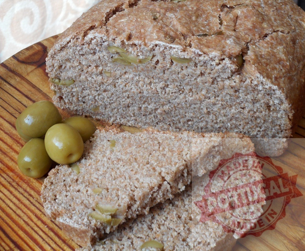 Whole wheat olive bread loaf with fresh ingredients | Rustic homemade olive bread loaf baked and sliced on a wooden board with green olives - Realized with Pictrs.com