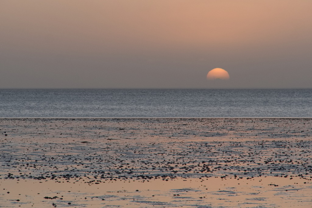 Sonnenaufgang über dem Watt | Die Sonne geht hinter leichtem Dunst über dem Watt auf. - Realisiert mit Pictrs.com