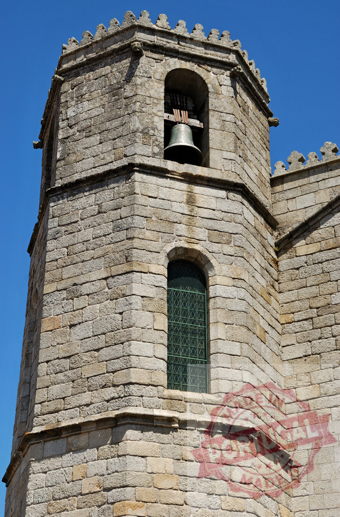 Historic bell tower with medieval stone architecture and blue sky. Region Norte - Portugal | Stone bell tower featuring a bell, arched window, and detailed stonework against a clear sky - Realized with Pictrs.com