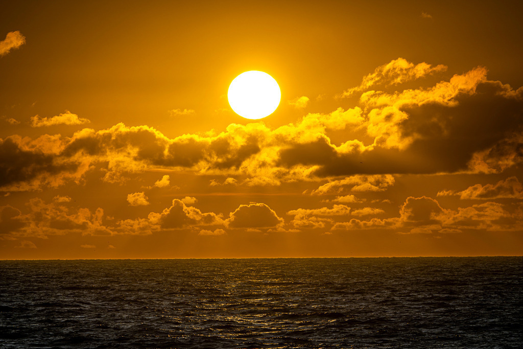 Leuchtender Sonnenuntergang über der Nordsee bei Texel | Strahlende Abendsonne bricht durch eine dichte Wolkenschicht über der Nordsee vor der Küste der niederländischen Insel Texel. Das grelle Licht taucht den Himmel in ein intensives Orange-Gold, während sich die untergehende Sonne auf der dunklen Wasseroberfläche spiegelt. Redaktionell vielseitig einsetzbar für Naturaufnahmen, Reiseberichte, Stimmungsbilder und Illustrationen zum Thema Küstenlandschaft, Urlaub und Abendstimmung. - Realisiert mit Pictrs.com