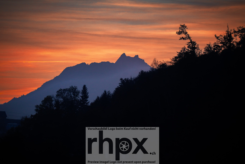 Pilatus Silhouette im leuchtenden Abendrot | <p><strong>Farbe. Stille. Gipfel.</strong></p><p>Die markante Silhouette des Pilatus zeichnet sich scharf gegen einen Himmel in intensiven Orange- und Rottönen ab. Der Aufstieg des Tages in die Nacht hult die Landschaft in ein dramatisches, friedvolles Lichtspiel.</p><p>Wahle unter "Produktauswahl" dein Wunschformat: Vom klassischen Wandbild uber Puzzle & Tassen bis zum digitalen Download (z.B. als Handy-Hintergrund).</p><br> - Realisiert mit Pictrs.com