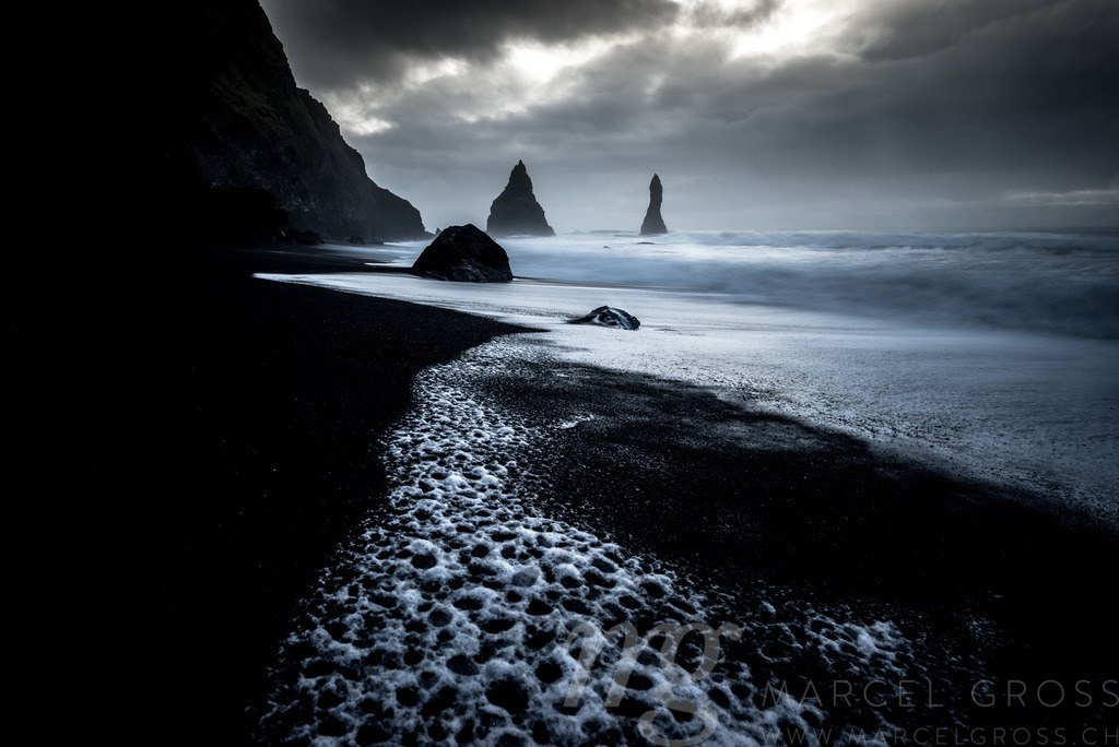 dark vulcanic beach | Reynisfjara is a famous, black sand beach near Vík í Mýrdal. But be careful, big waves may occur any time and have taken to many lifes. In the distance you can see the rock needles of Reynisdrangar. - Realisiert mit Pictrs.com