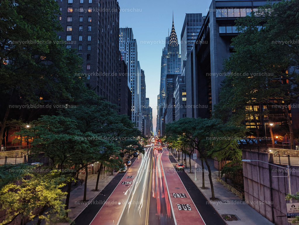 Blaue Stunde in Midtown – Blick von der Tudor City Bridge auf das Chrysler Building mit Lichtspuren der Autos | Die blaue Stunde legt sich wie ein sanfter Schleier über Midtown Manhattan. Vom Geländer der Tudor City Bridge aus öffnet sich ein magischer Blick: Das Chrysler Building glänzt wie ein Juwel, während die Lichtspuren der Autos durch die Straßen fließen – ein lebendiger Rhythmus, eingefangen an einem warmen Sommerabend bei 29 Grad.