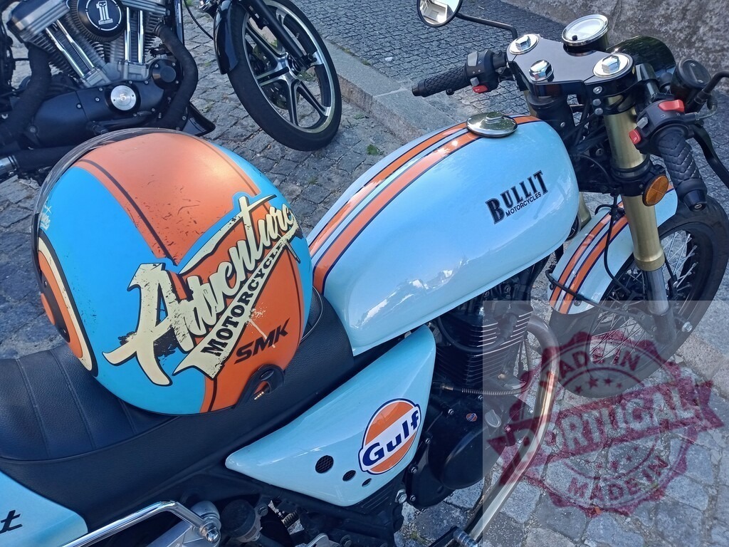 Bullit motorcycle with adventure helmet resting on seat | Light blue vintage Bullit motorcycle with Gulf logo and orange and blue SMK adventure motorcycle helmet resting on the black seat - Realized with Pictrs.com