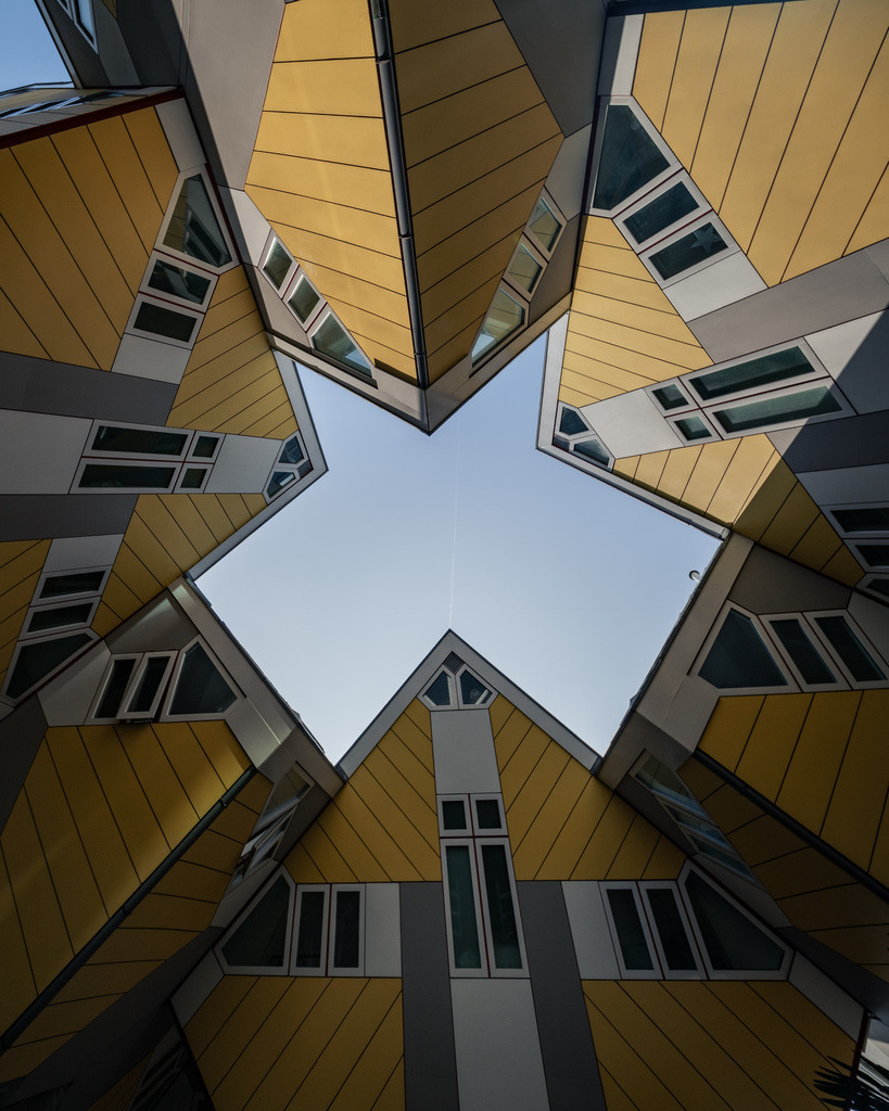 Symmetrischer Blick in den Himmel zwischen Rotterdams Kubushäusern | Die markanten Kubushäuser in Rotterdam bilden aus der Froschperspektive eine nahezu sternförmige Komposition rund um den blauen Himmel. - Realisiert mit Pictrs.com