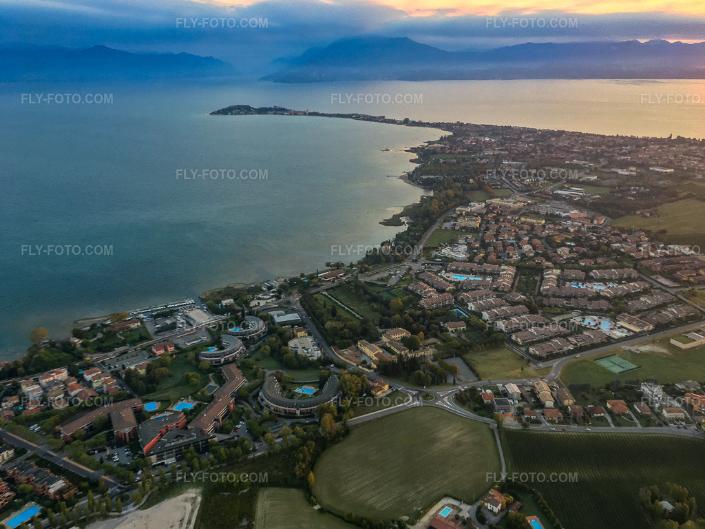 Aerial view: Sirmione peninsula on Lake Garda in the morning light in Desenzano del Garda in the state Brescia, Italy. – Photo: IMG-134980.jpg taken on 09/23/2022 by Werner Riehm/FLY-FOTO.com – Resolution of the original: 3910 x 2932 px