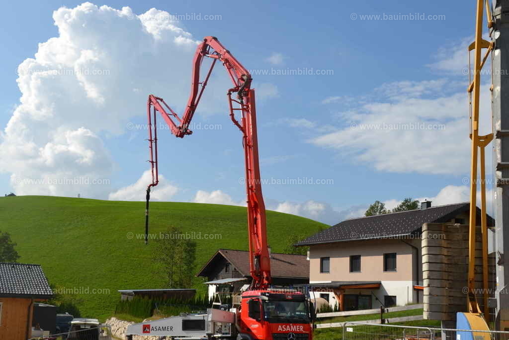 Autobetonpumpe | Betonpumpe mit mehrfach geknicktem Ausleger, dahinter grüne Landschaft mit blauem Wolkenhimmel