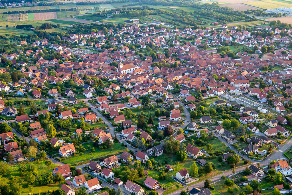Aerial view: View of the town from the southwest in Bischoffsheim in the state Bas-Rhin, France. – Photo: IMG_137977.jpg taken on 08/19/2023 by Werner Riehm/FLY-FOTO.com – Resolution of the original: 5167 x 3444 px