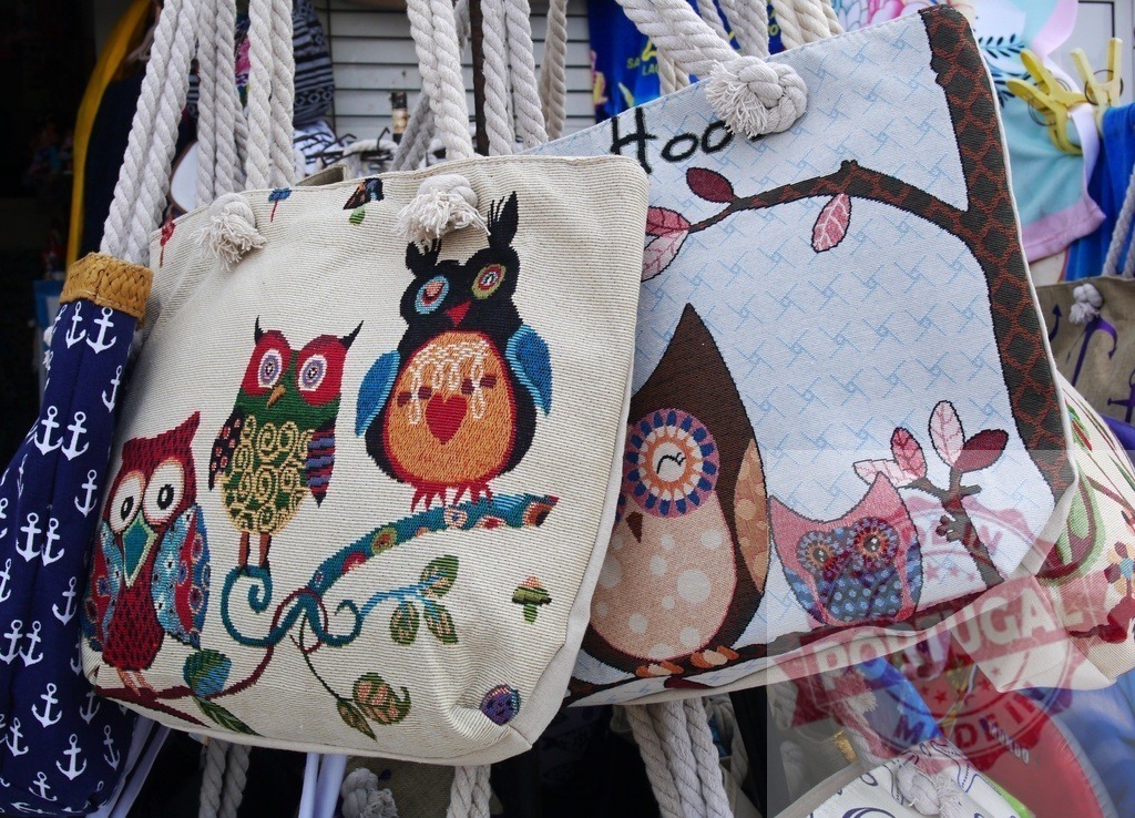 Colorful owl tote bags hanging on display for sale | Colorful canvas tote bags with embroidered owl designs and rope handles are on display - Realisiert mit Pictrs.com