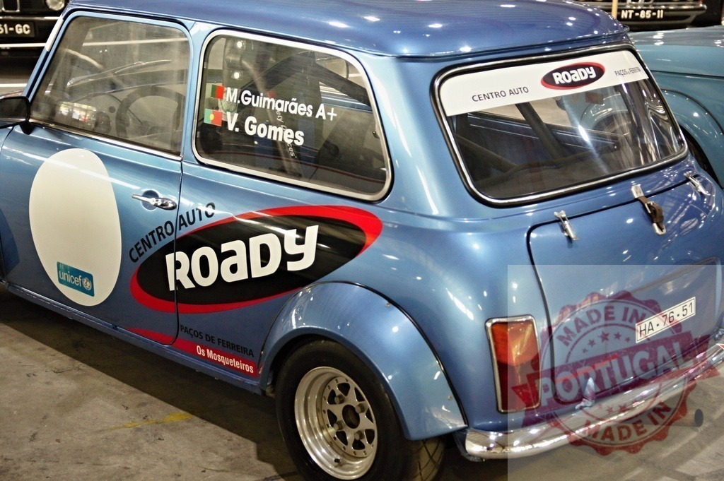 Classic Mini Cooper showcasing UNICEF and Roady sponsorships at car show | Light blue vintage Mini Cooper on display, highlighting UNICEF and Roady branding at an indoor automotive exhibition - Realized with Pictrs.com