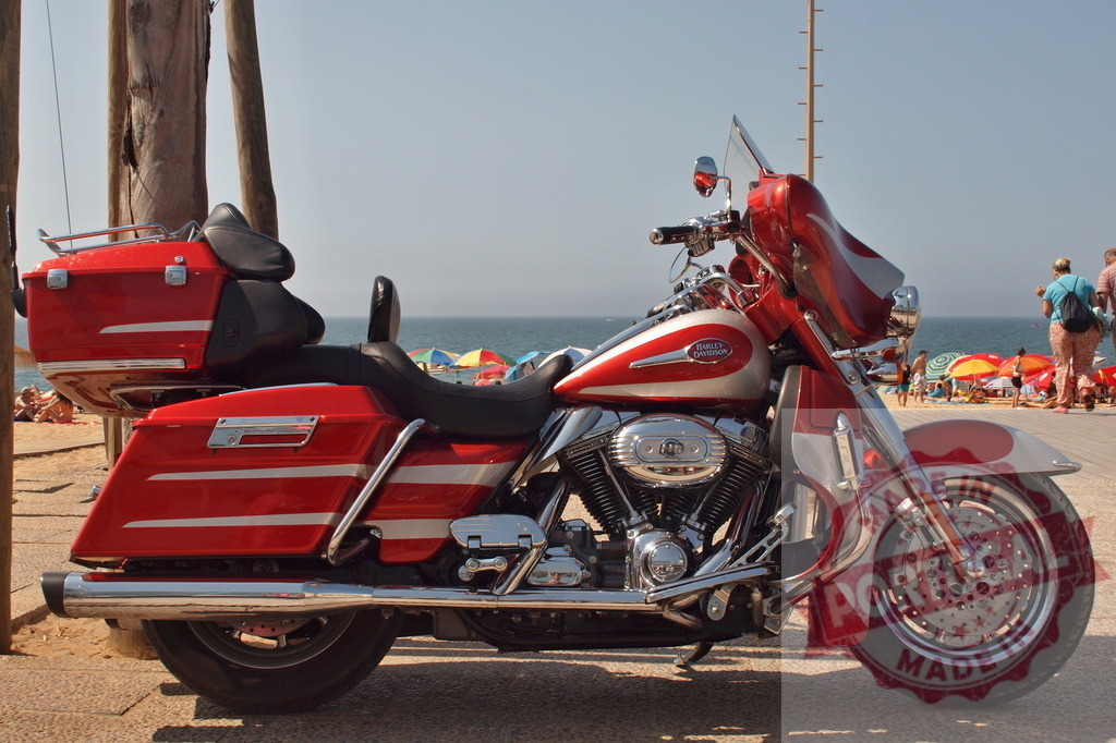 Harley-Davidson motorcycle parked on a sunny beach boardwalk | Red and white Harley-Davidson motorcycle parked by the ocean with beach umbrellas in the background - Realized with Pictrs.com