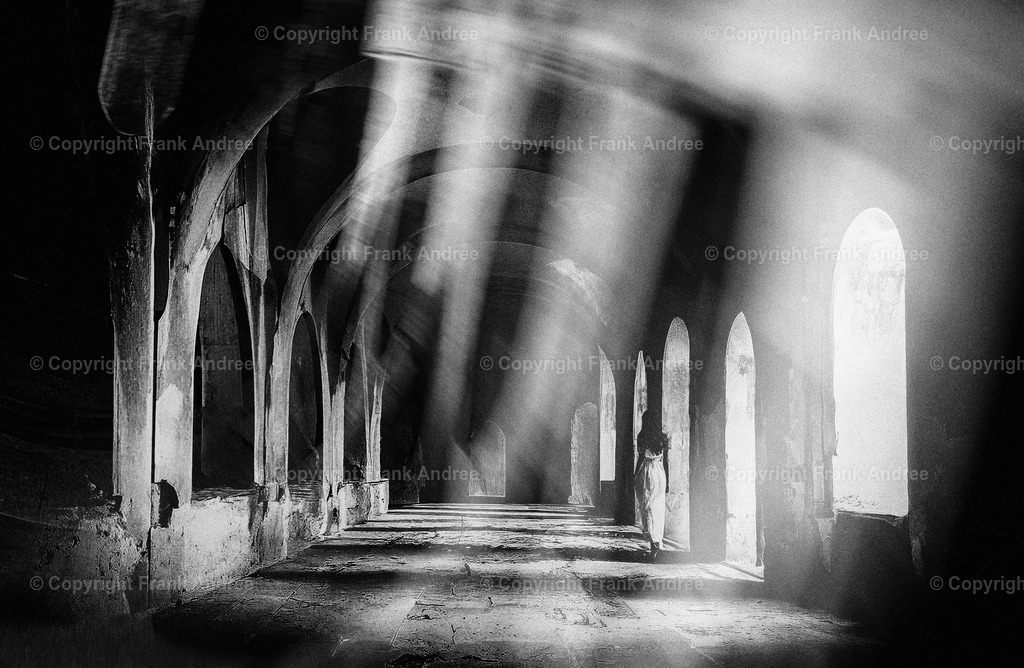 Illusion 3 | Eine Frau im weißen Kleid geht allein durch ein lichtdurchflutetes altes Gewölbe. Digitale Kunst in schwarz weiß - Realisiert mit Pictrs.com