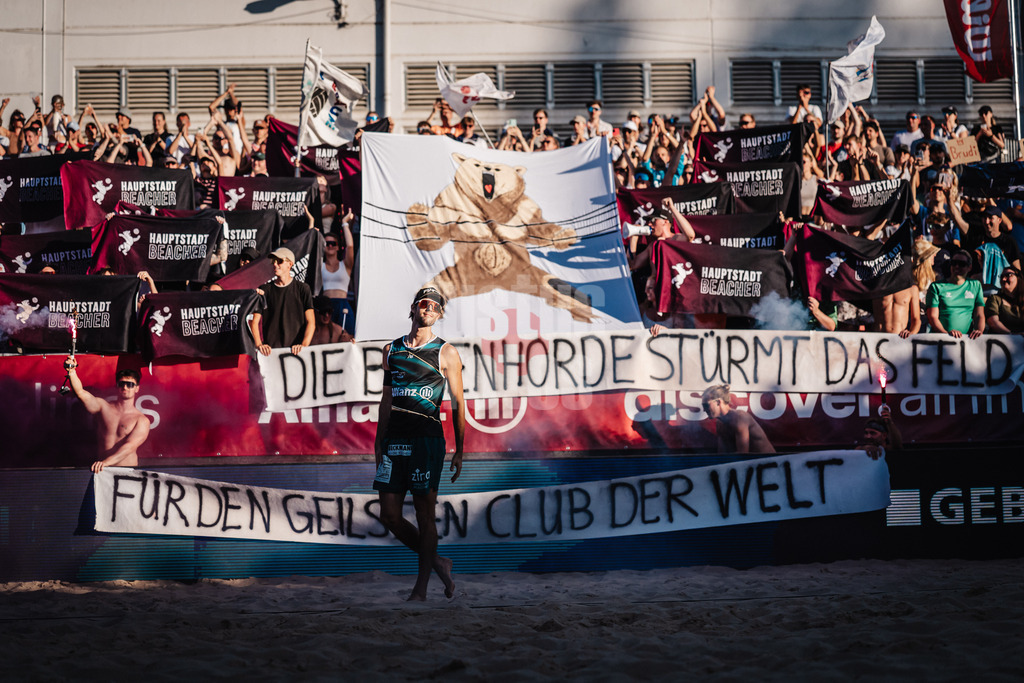 Beachvolleyball | Männer | Allianz German Beach Tour 2025 | Tourstop Berlin | 16.08.2025 | Vorne Niklas Held, dahinter eine Choreografie der Fangruppe Fraktion Bräune mit Pyrotechnik und einem Transparent mit der Aufschrift Die Bärenhorde stürmt das Feld für den Geilsten Club der Welt