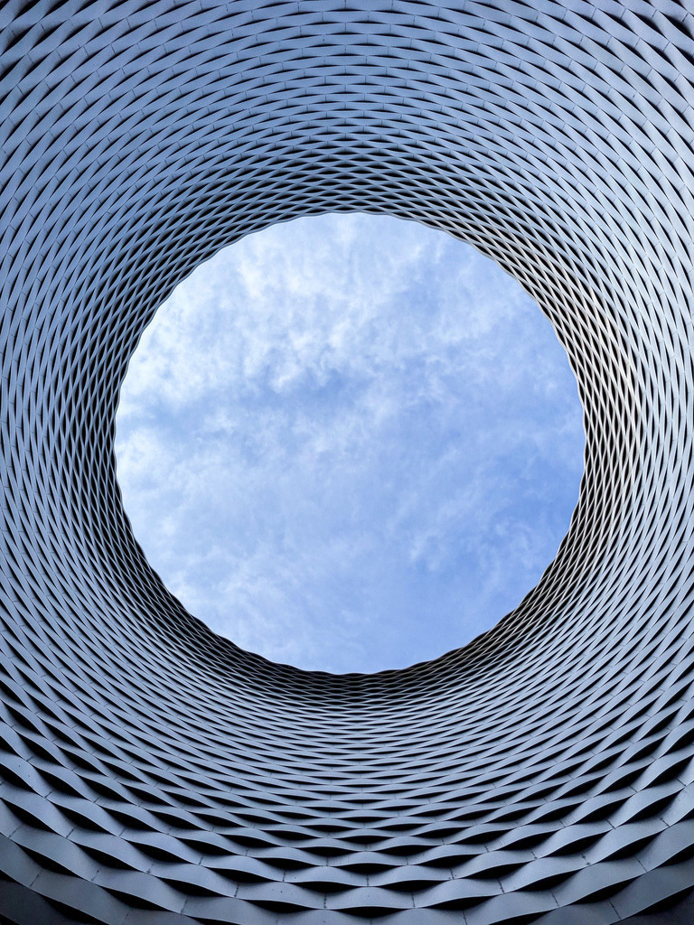 Messe Basel Oculus | Das Fenster zum Himmel | Abstrakte Architekturfotografie des berühmten Deckenkreisels der Messe Basel, entworfen von Herzog &amp; de Meuron. Diese spektakuläre Öffnung wird auch liebevoll „Das Fenster zum Himmel“ genannt und fängt hier vorbeiziehende Wolken in perfekter Geometrie ein. Elegante Wandkunst für moderne Räume. / Modern architecture of the Messe Basel oculus. - Realisiert mit Pictrs.com