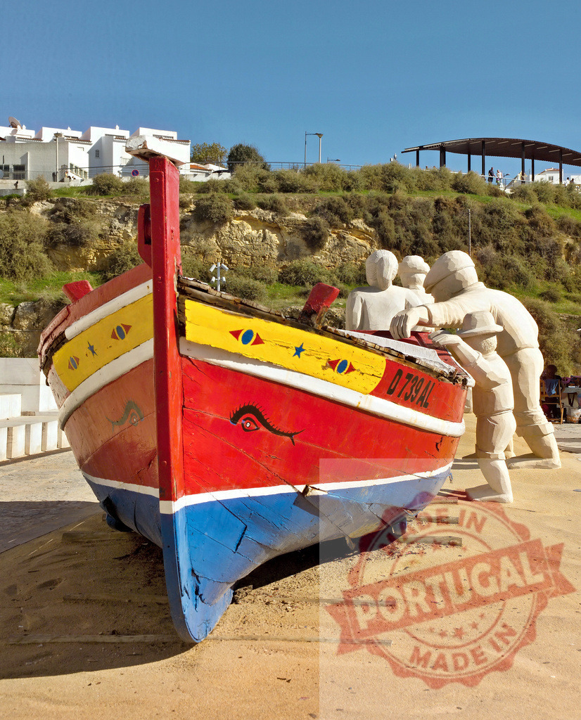 Traditional Portuguese fishing boat and fishermen sculpture | Colorful old boat with traditional fishermen sculptures on the sand in a coastal town - Realisiert mit Pictrs.com