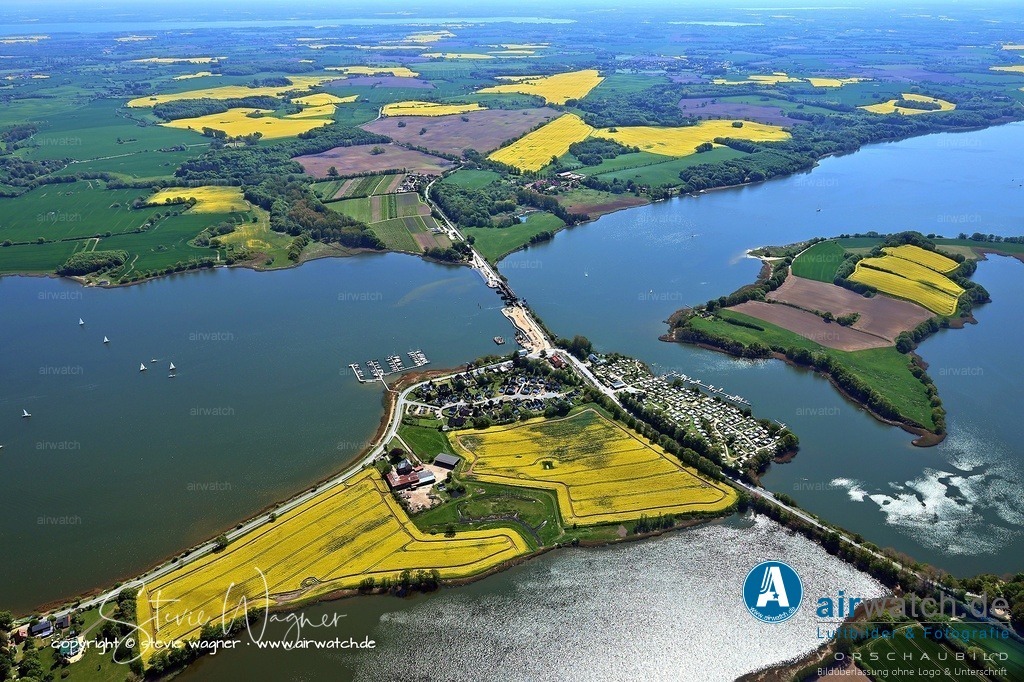 Luftbild Ostseefjord Schlei, Boren-Lindaunis Schleibrücke, Campingplatz Lindaunis, Sportboothafen Lindaunis | Lindaunis, ein Ortsteil der Gemeinde Boren in Schleswig-Holstein, liegt an der Schlei und ist bekannt für seine historische Klappbrücke, die seit 1927 den Meeresarm Schlei an einer der schmalsten Stellen überspannt und bis 2021 für Eisenbahnen und Kraftfahrzeuge genutzt wurde. Seitdem ist die Brücke nur noch zu Fuß überquerbar, da sie abgebaut und durch einen Neubau ersetzt wird.