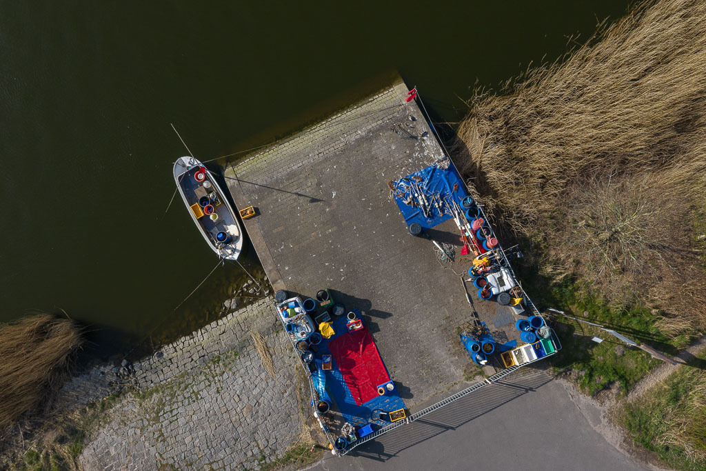 zeitenwende-farbe-03-01 | Blick auf die Ersatzübergangsstelle ("NATO-Rampe") in Missunde an der Schlei aus einer Höhe von 24 Metern. Diesen Platz nutzt der Schleifischer Matthias Nanz als Anleger für seine Boote, als Lager und als Verkaufsstelle für seinen Tagesfang. - Realisiert mit Pictrs.com