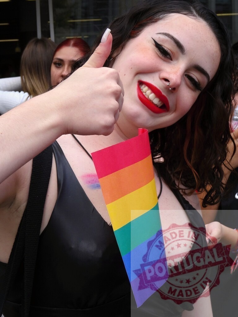 Young woman showing pride with rainbow flag, thumbs up | Smiling young woman showing thumbs up and holding a rainbow flag during a pride parade - Realized with Pictrs.com