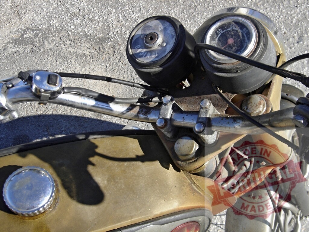 Close-up of rusty vintage motorcycle handlebar showing speedometer and fuel tank | Rusty vintage motorcycle handlebar with speedometer, fuel tank, and visible electrical wires, suggesting age and disuse - Realized with Pictrs.com