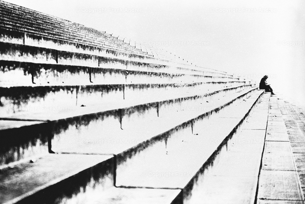 Die Leserin | Eine Frau sitzt allein auf einer Steintreppe und liest ein Buch. Straßenfotografie aus Berlin in schwarz und weiß. - Realisiert mit Pictrs.com