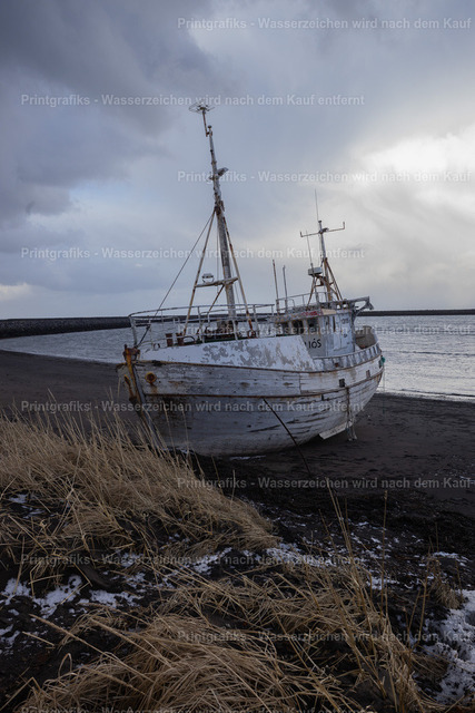 Gestrandetes Boot an Islands Küste | Ein altes, verwittertes Boot liegt am schwarzen Strand vor der rauen Küste Islands. Der dunkle Sand, das trockene Gras, die Schneereste und der schwere Himmel erzeugen eine stille, melancholische Stimmung nordischer Einsamkeit. - Realisiert mit Pictrs.com