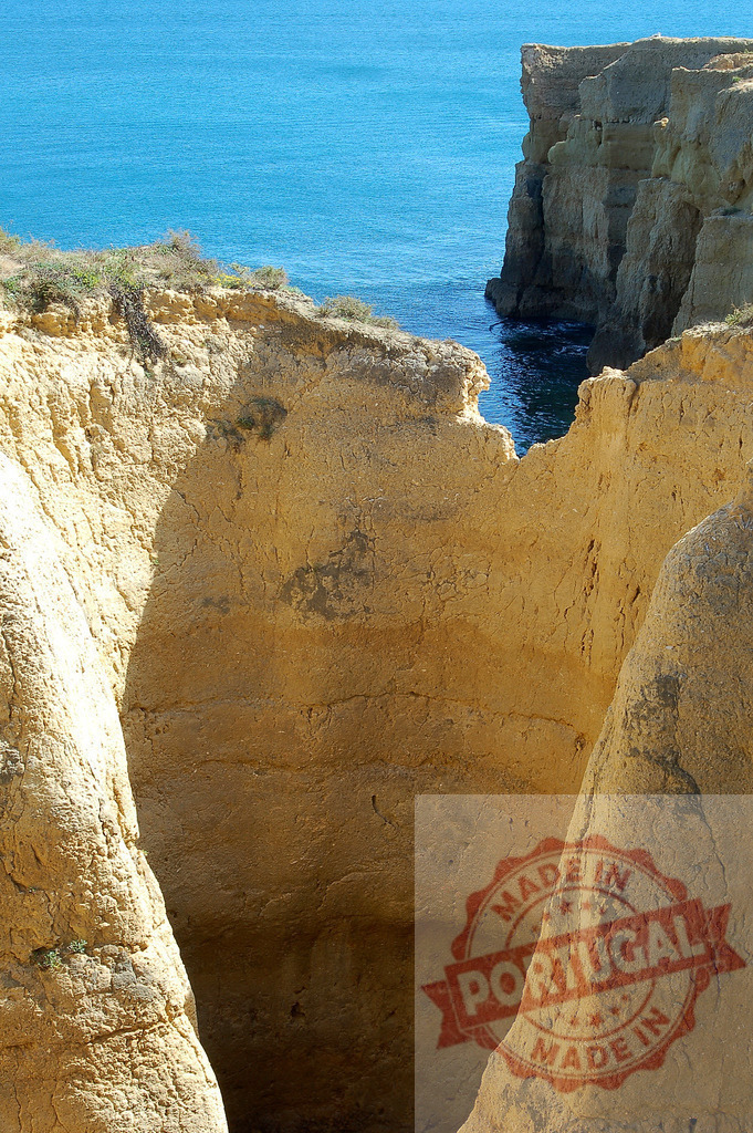 Coastal cliff erosion creating natural rock formations | Sandy cliffs carved by erosion frame the blue ocean, forming a natural arch and grotto entrance - Realized with Pictrs.com
