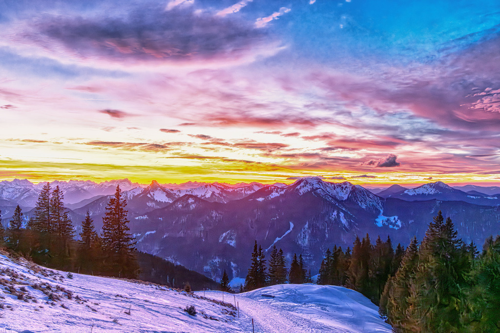 Idyllischer winterlicher Sonnenuntergang in den bayrischen Alpen am Tegernsee | Das Bild zeigt eine idyllische Winterlandschaft in den bayrischen Alpen am Tegernsee.Motiv: Ein verschneites Panorama-Gebirge mit Nadelwäldern bei Sonnenuntergang.Atmosphäre: Die Wolken sind in ein intensives Violett- und Orangegelb getaucht, typisch für das Alpenvorland im Winter.Aktivitäten: Solche Szenen sind typisch für Regionen, die zum Skifahren, Schneeschuhwandern oder Langlaufen einladen.  - Realisiert mit Pictrs.com