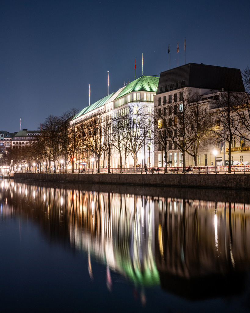 Hotel Vier Jahreszeiten an der Binnenalster bei Nacht | Das beleuchtete Hotel Vier Jahreszeiten am Neuen Jungfernstieg spiegelt sich in der ruhigen Binnenalster und prägt die nächtliche Hamburger Stadtkulisse. - Realisiert mit Pictrs.com